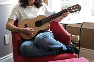 A player fingerpicking the Ventura in an armchair at home